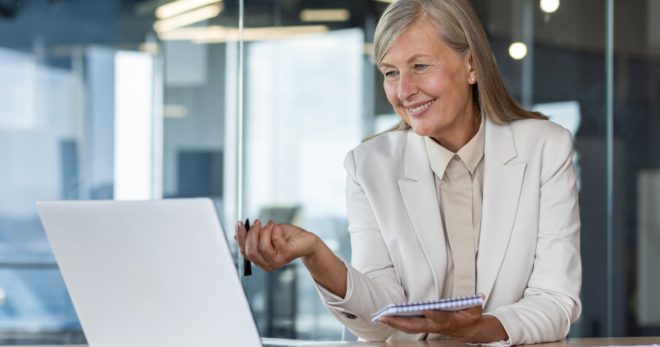 woman smiling at computer with pen and notepad in hand